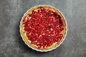 Redcurrant cheesecake, tart with fresh berries in a white baking dish on dark gray background. Top view. photo