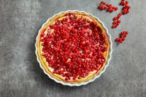 Redcurrant cheesecake, tart with fresh berries in a white baking dish on dark gray background. Top view. photo