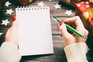 Top view of female hand writing in a notebook on wooden Christmas background. Wish list. New Year concept photo