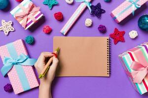 Top view of female hand making some notes in noteebok on colorful background. New Year decorations and toys. Christmas time concept photo