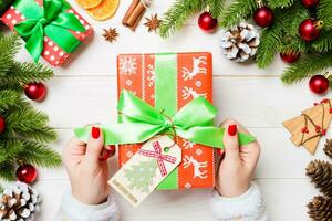 Top view of female hand tie up New Year present on festive wooden background. Fir tree and holiday decorations. Christmas time concept photo