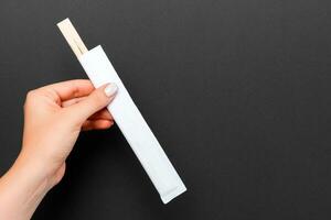 Crop image of female hand holding chopsticks on black background. Japanese food concept with copy space photo