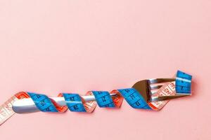 Diet concept with fork wrapped in measuring tape on pink background. Top view of weight loss with empty space photo