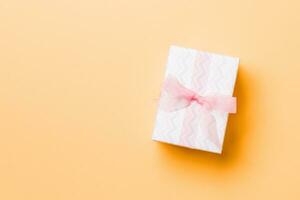 wrapped Christmas or other holiday handmade present in paper with pink ribbon on orange background. Present box, decoration of gift on colored table, top view with copy space photo