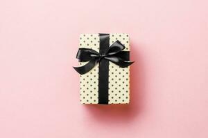 Gift box with black bow for Christmas or New Year day on pink background, top view with copy space photo