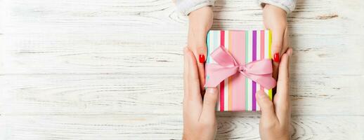 Top view of two people sharing a present on wooden background. Holiday and surprise concept. Copy space photo