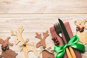 Top view of new year utensils on napkin with holiday decorations and reindeer on wooden background. Christmas dinner concept with copy space photo