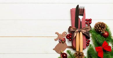 Top view of holiday objects on wooden background. Utensils tied up with ribbon Banner on napkin. Christmas decorations and reindeer with copy space. New year dinner concept photo