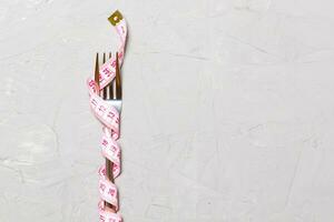 Close up of fork wrapped with tape measure on gray background. Top view of obesity concept photo