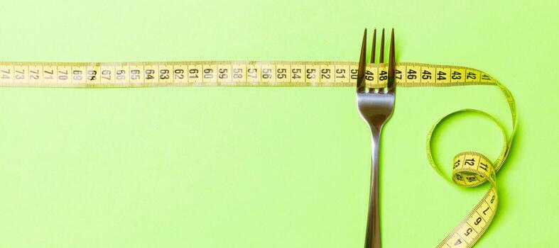 Fork with curled tape measure on green background. Top view of ftatware. Dietary concept with space for your design photo