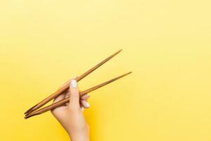 Female hand with chopsticks on yellow background. Traditional asian food with emty space for your design photo