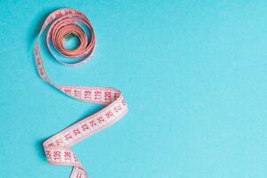 Top view of curled measuring tape as a sewing accessory on blue background. Tailor concept with copy space photo