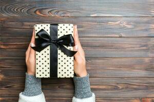 Female's hands holding striped gift box with colored ribbon on dark rustic wooden background. Christmas concept or other holiday handmade present box, concept top view with copy space photo