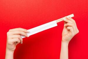 Crop image of two female hands holding chopsticks on red background. Ready to eat concept with copy space photo