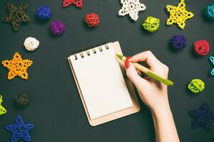Top view of female hand making some notes in noteebok on colorful background. New Year decorations and toys. Christmas time concept photo
