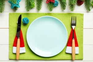 Top view of fork, knife and plate surrounded with fir tree and Christmas decoratoins on wooden background. New Year Eve and holiday dinner concept photo