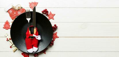 Holiday composition of plate and flatware decorated with Santa clothes on wooden background. Banner Top view of Christmas decorations with empty space for your design. Festive time concept photo