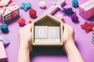 Top view of female hands holding calendar on purple background. The first of January. Holiday decorations. New Year concept photo