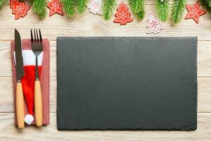 Top view of Christmas dinner on wooden background. Plate, utensil, fir tree and holiday decorations with copy space. New Year time concept photo