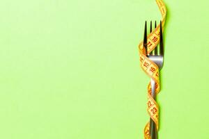 Fork wrapped in measuring tape on green background. Top view of overeating concept photo