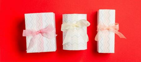 wrapped Christmas or other holiday handmade present in paper with Colored ribbon on red background. Present box, decoration of gift on colored table, top view photo