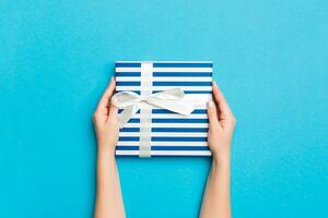 Woman arms holding gift box with colored ribbon on blue table background, top view and copy space for you design photo