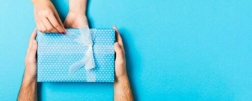 Top view of a present in male and female hands on colorful background. Congratulating of each other concept. Close up photo