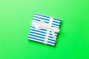 wrapped Christmas or other holiday handmade present in paper with white ribbon on green background. Present box, decoration of gift on colored table, top view with copy space photo