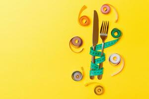 Top view composition of fork and knife with colored balled measuring tapes on yellow background with empty space for your ideas. Overweight and overeating concept photo