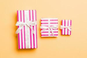 wrapped Christmas or other holiday handmade present in paper with White ribbon on orange background. Present box, decoration of gift on colored table, top view photo