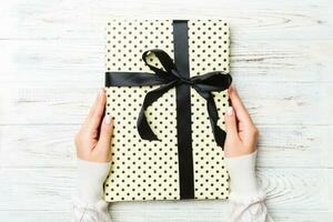 Female's hands holding striped gift box with colored ribbon on white rustic wooden background. Christmas concept or other holiday handmade present box, concept top view with copy space photo