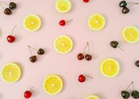 Creative fruit pattern made of red cherries and yellow lemon slices on light pastel pink background. Minimal cherry fruit and citrus layout. Nature summer pattern concept. Flat lay summer food idea. photo