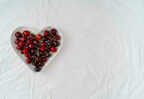 Creative love layout in shape of a heart made of red cherries. Minimal summer fruit concept. Flat lay love idea. Cherry aesthetic. Copy space. photo