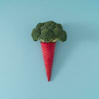 Pink waffle ice cream cone with broccoli on light blue background. Minimal food concept. Summer creative idea. Yummy vegetable layout. Ice cream flat lay composition. photo