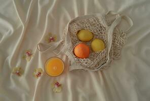 Flat lay orange juice and lemons in crochet net bag on sandy silk background. Summer fruit aesthetic idea. Minimal creative concept. photo