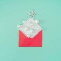 Creative composition made of Christmas baubles coming out of red envelope on pastel green background. Minimal Christmas or New Year concept. Trendy winter holidays idea. Flat lay, top of view. photo
