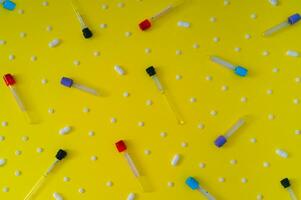 Pattern made of blood test sample tubes and white pills on yellow background. Medical laboratory testing, analysis and research idea. Creative minimal biochemistry, science and pharmacy concept. photo