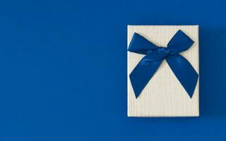 Closeup view minimal composition of Christmas gift box on blue backdrop with copy space. New Year present concept background. Trendy gift box idea. Gift box aesthetic layout. Flat lay. photo