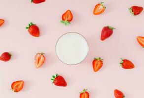 Creative pattern composition made of milk drink with strawberry taste in glass cup and red strawberries on pastel pink background. Minimal smoothie or milkshake concept. Healthy food for breakfast. photo