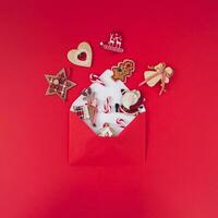 Creative composition made of various Christmas objects coming out of red envelope on red background. Minimal Christmas or New Year concept. Trendy winter holidays idea. Flat lay, top of view. photo