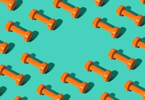 Creative pattern composition made of orange dumbbells on pastel green background with copy space. Minimal fitness, healthy lifestyle and sport concept. Trendy exercise and fitness backround idea. photo