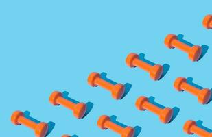 Creative pattern composition made of orange dumbbells on light blue background with copy space. Minimal fitness, healthy lifestyle and sport concept. Trendy exercise and fitness backround idea. photo