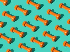 Creative pattern composition made of orange dumbbells on pastel green background. Minimal fitness, healthy lifestyle and sport concept. Trendy exercise and fitness backround idea. photo