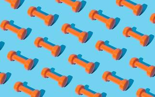 Creative pattern composition made of orange dumbbells on light blue background. Minimal fitness, healthy lifestyle and sport concept. Trendy exercise and fitness backround idea. photo