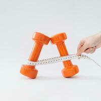 Creative composition made of orange dumbbells and  measuring tape on white background. Minimal fitness, healthy lifestyle and sport concept. Trendy exercise and fitness idea. photo