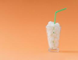 Creative composition made of glass full of sugar cubes with green drinking straw on pastel orange background. Minimal unhealthy diet concept. Be healthy lifestyle idea. Copy space. photo