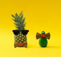 Creative and funny composition made of fresh pineapple and avocado with sunglasses and wooden bow tie on yellow background. Minimal exotic fruit concept. Trendy food idea. Tropical fruit aesthetic. photo