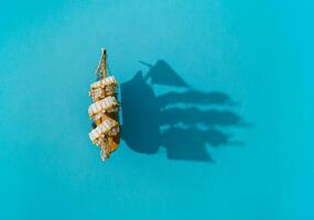 Old ship traveling on the sea. Sailing boat and shadow on blue background composition. Travel, vacation and summer journey concept. Flat lay summer sailboat and shadow idea. Copy space. photo