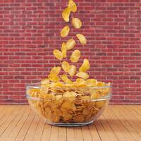 Creative layout made of healthy corn flakes falling into glass bowl against red brick wall background. Minimal breakfast food concept. Fancy breakfast cereal idea. Cornflakes aesthetic. photo