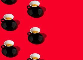 Trendy pattern made of black cup of coffee on red background with copy space. Creative coffee concept. Minimal espresso pattern idea. Coffee aesthetic. photo